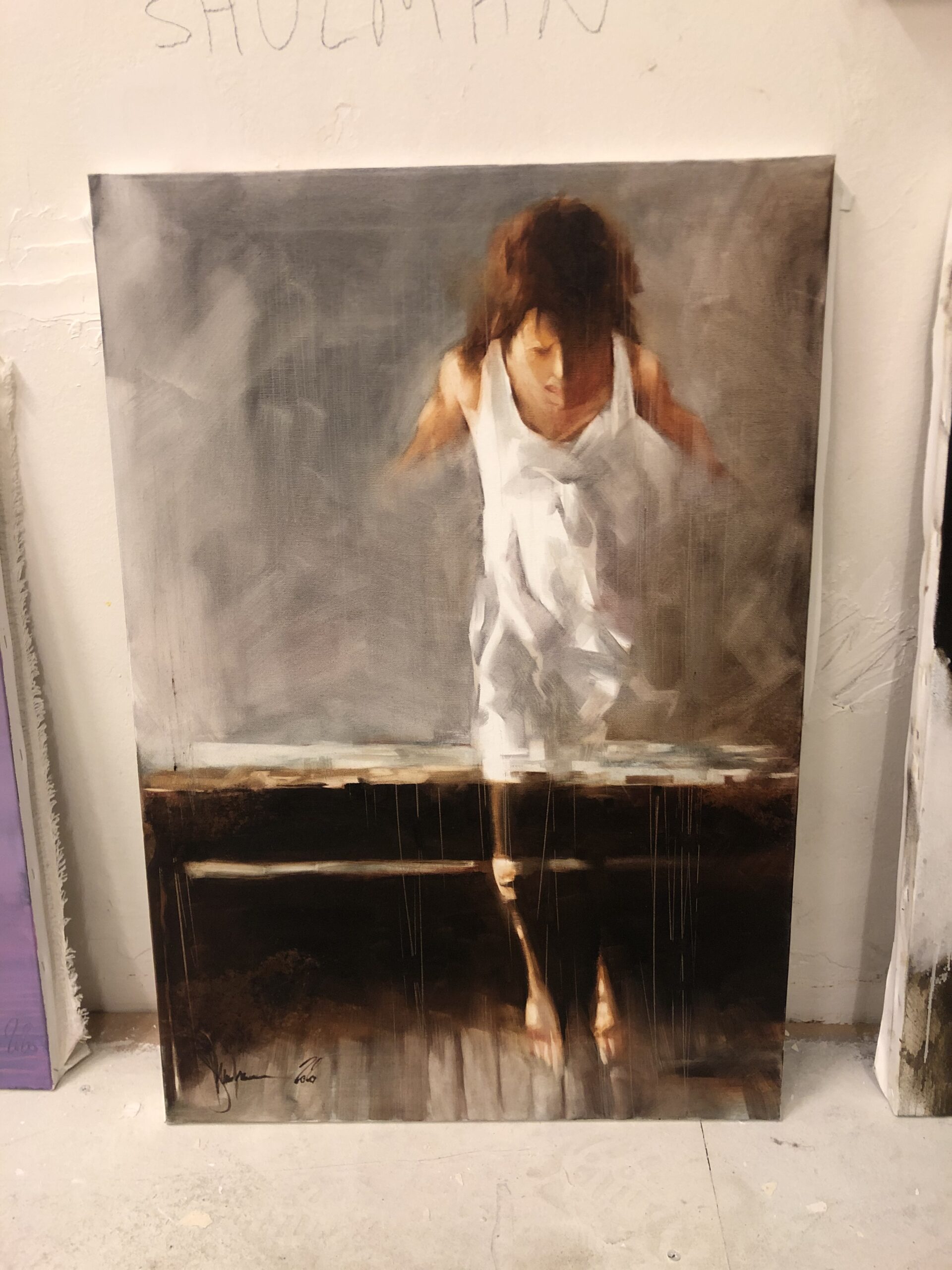 A young woman in a simple white dress sits in quiet contemplation, her figure softly rendered against a muted, indistinct background.