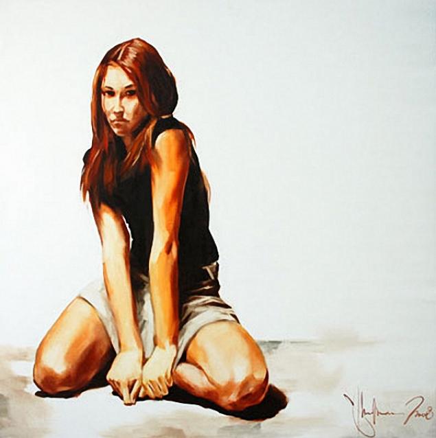 Young woman with long auburn hair kneeling on a light floor, wearing a black sleeveless top and light skirt, gazing seriously at the viewer.