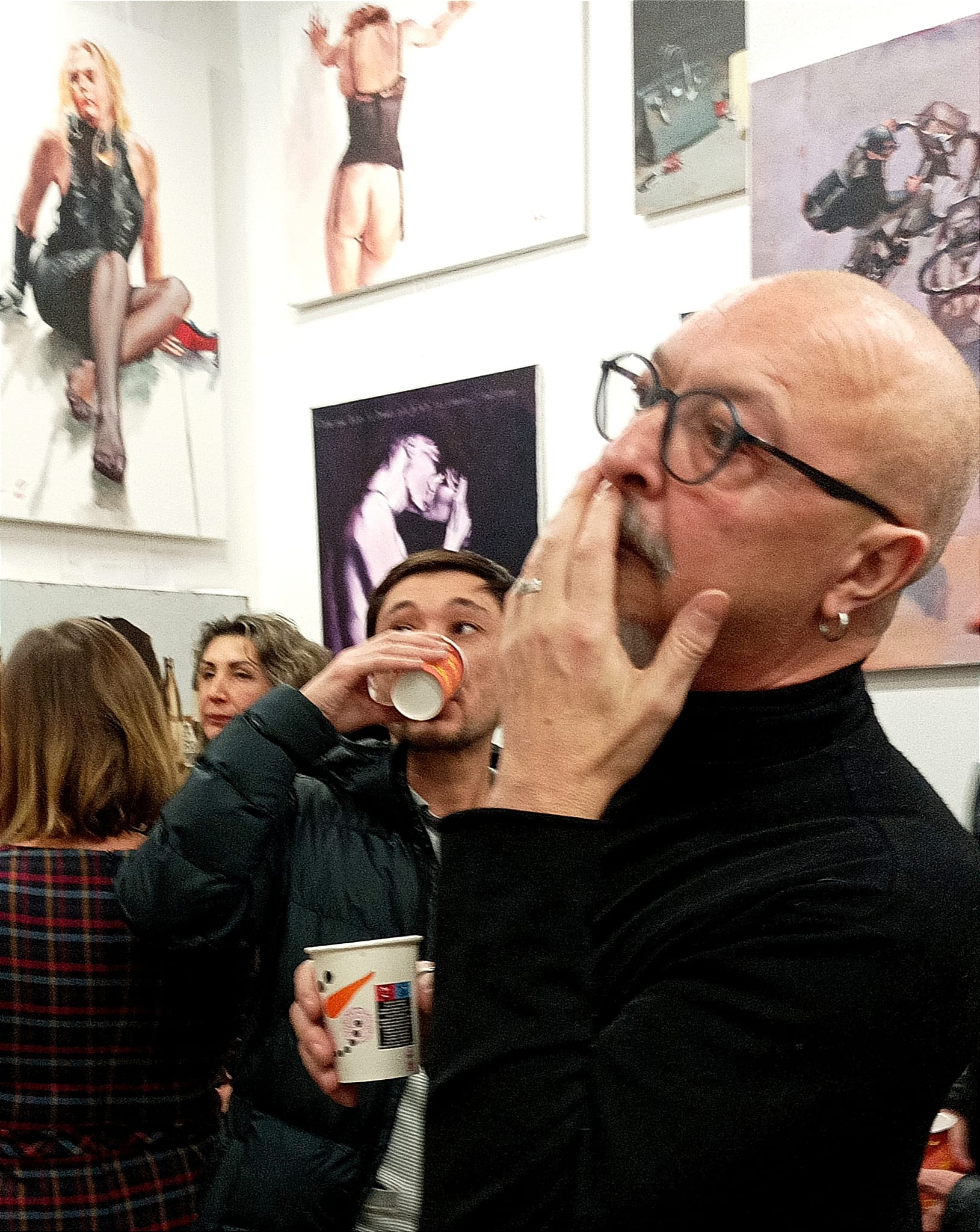 Igor Shulman standing in ART Gallery 11 Prague surrounded by his paintings including Meeting After Work, Red Lipstick, Unexpected Developments, and I Love You