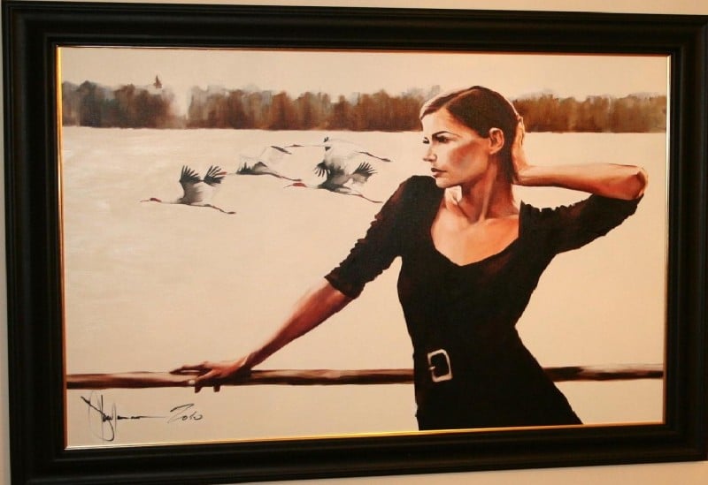 Oil painting "Winter Morning" by Igor Shulman featuring a woman in a black dress gazing contemplatively at a flock of cranes in flight over a tranquil winter landscape, 90 x 120 cm.
